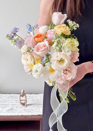 Hand-tied bridal bouquet featuring pink roses, quicksand rose, and soft pastel flowers for weddings.