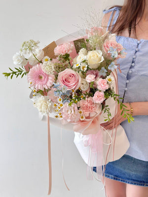 Person holding a bouquet of pink and white flowers against a plain background