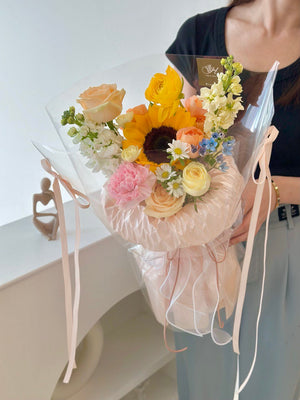1. A happy graduate woman holds a sunflower bouquet in a clear bag, celebrating her achievement with a gift from a friend.
2. A joyful woman in graduation attire holds a sunflower bouquet in a clear bag, expressing happiness for her friend's gift.
3. A smiling graduate holds a clear bag containing a sunflower bouquet, celebrating her graduation with a thoughtful gift from a friend.