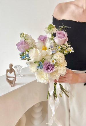 A bride holds a bouquet of white and Lilac flowers, featuring purple ROM flowers and tulips for her wedding.