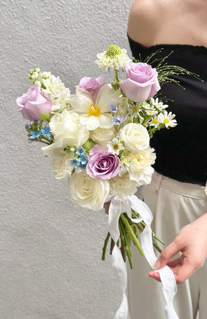 A bride displays a bouquet of white and lilac flowers, including purple ROM flowers and white tulips, on her wedding day.