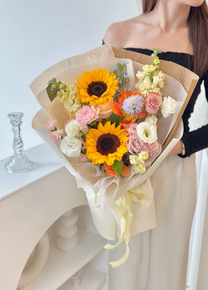A joyful graduate woman displays a bouquet of sunflowers and mixed flowers, symbolizing her graduation celebration.