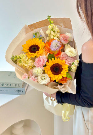 A graduate girl proudly holds a bouquet of sunflowers and mixed flowers at her graduation ceremony.