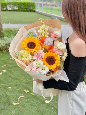 A girl in graduation attire holds a vibrant bouquet of sunflowers and assorted flowers, celebrating her achievement.
