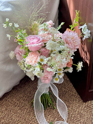 Bouquet of pink and white flowers with a white ribbon on a carpeted floor.
