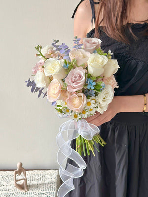 Soft pastel wedding bouquet with white roses, chamomile flowers, and eucalyptus leaves held by bride in black dress.