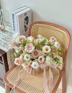 Bouquet of flowers in a basket on a wicker chair with a book in the background.