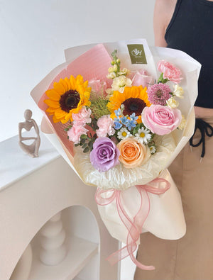 A woman dressed in a black gown holds a graduation bouquet, reflected in a mirror at her graduation ceremony.