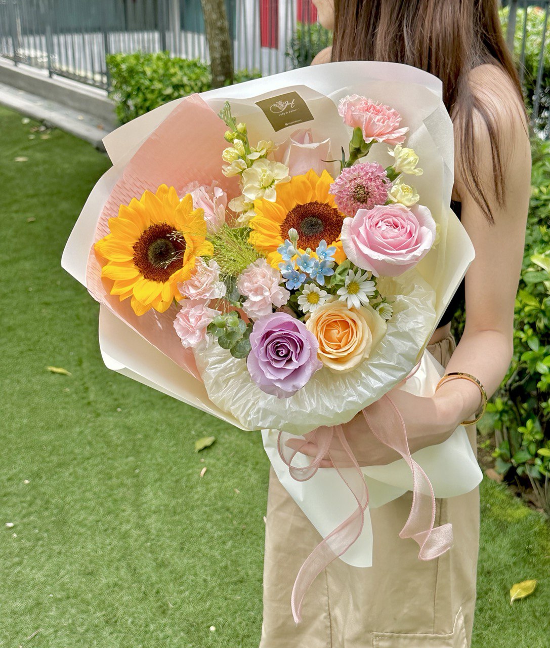 A graduate in a black gown admires her bouquet of flowers during her graduation ceremony at her university.