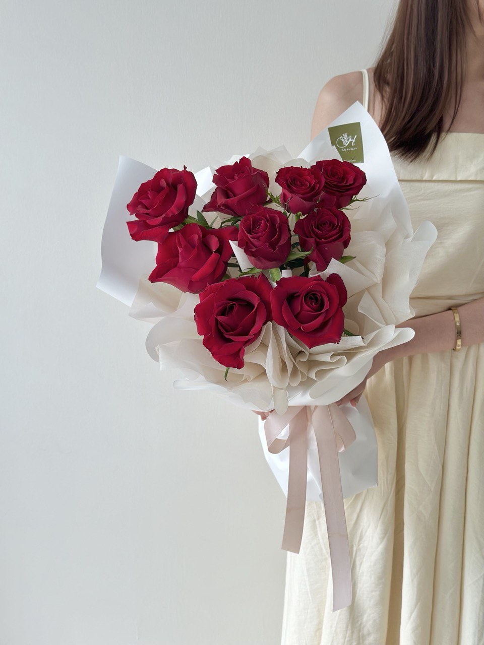 Bouquet of red roses held by a person wearing a beige dress on a light gray background for Valentine's Day.