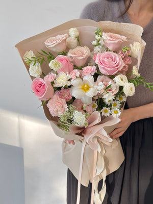 Bouquet of pink and white flowers held by a person against a neutral background