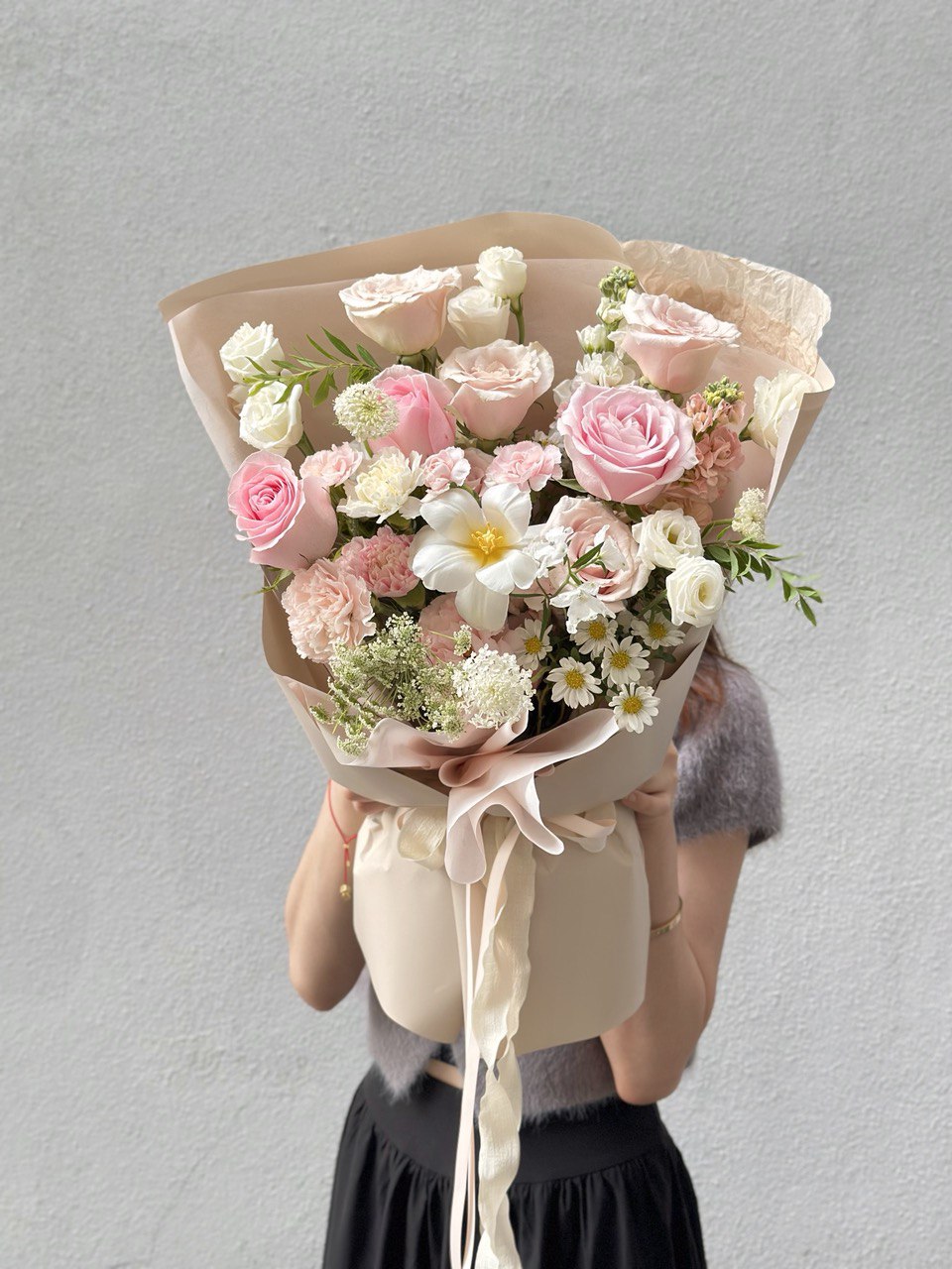 Bouquet of pink and white flowers held by a person against a gray background