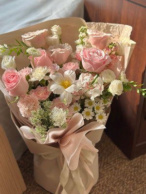 Bouquet of pink and white flowers in a decorative paper wrap on a wooden surface.
