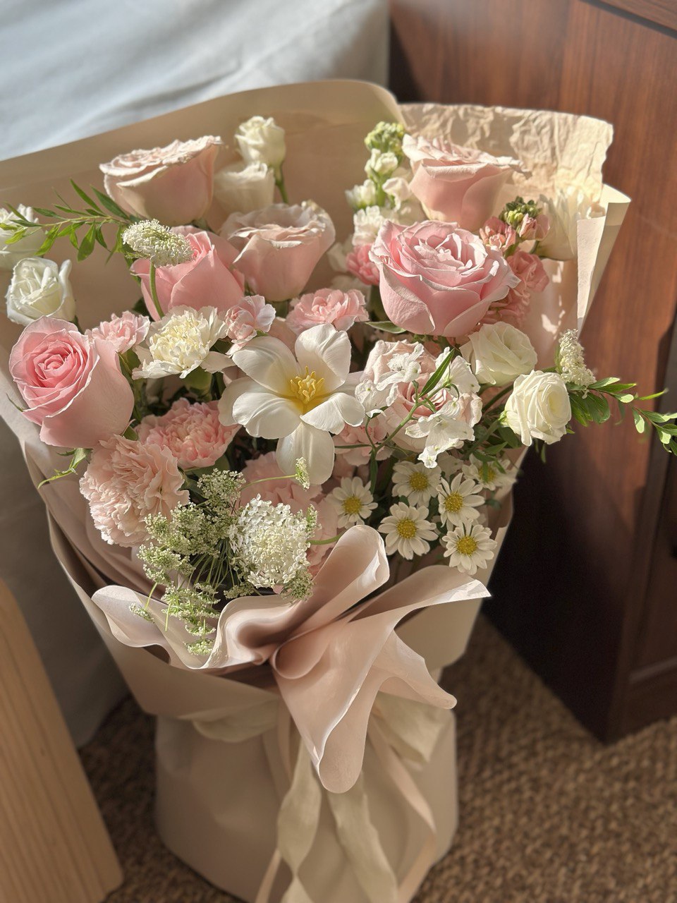 Bouquet of pink and white flowers in a decorative paper wrap on a wooden surface.