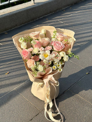 Soft-toned flower bouquet with layered pink roses and white fillers, wrapped in beige and finished with flowing ribbon.