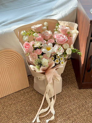 Elegant bouquet with soft pink roses, white tulip, and delicate chamomile flowers, place on a carpeted floor.