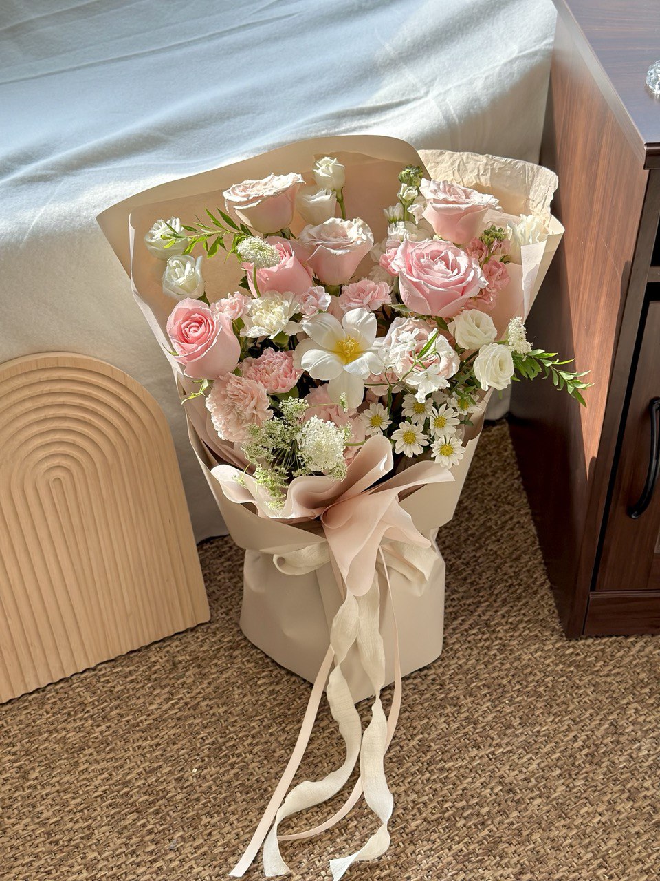 Elegant bouquet with soft pink roses, white tulip, and delicate chamomile flowers, place on a carpeted floor.