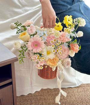 Close-up of a cheerful flower basket featuring gerbera, lisianthus, and chamomile, tied with cream ribbon on a jute mat.