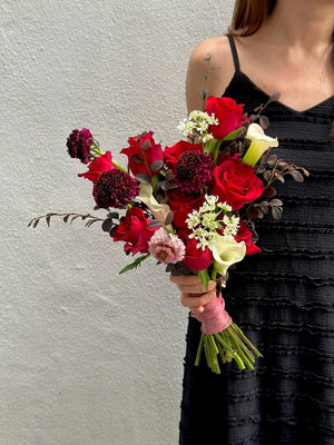 A woman dressed in black holds a bouquet of red roses mixed calla lilies, ready for her wedding ceremony.