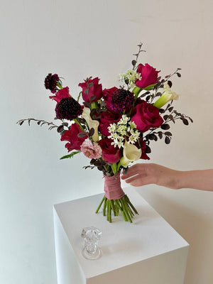 A girl hand is preparing to hold a vibrant bouquet of red roses mixed calla lilies, preparing for her wedding celebration.