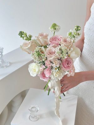 A woman in a white gown holds a stunning pink rose mixed quicksand rose bouquet, radiating joy on her wedding day at Kuala Lumpur.