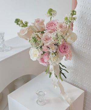 A woman in a white long dress holds a bouquet of Quicksand rose mixed with pink rose, celebrating her wedding day.
