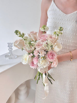 A bride in a white dress holds a beautiful bouquet of pink roses mixed with quicksand rose on her wedding da