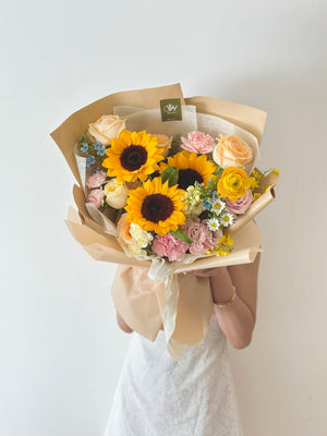A woman wearing a white dress holds a vibrant sunflower bouquet, marking her graduation from university.