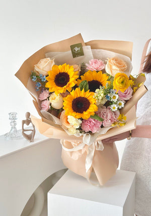 A graduate in a white dress proudly holds a bouquet of sunflowers, symbolizing her achievement.