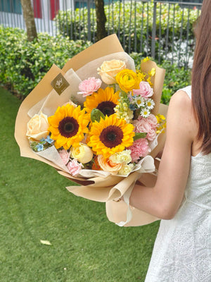 A woman in a white dress holds a sunflower bouquet, celebrating her university graduation.