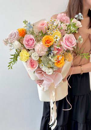 Elegant mixed-flower arrangement in warm tones, styled with flowing ribbons and delicate wrapping paper.