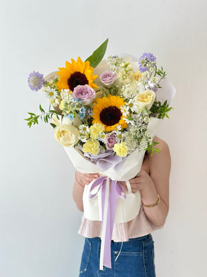 A hand-tied bouquet with sunflowers, roses, and mixed seasonal blooms, perfect for congratulating a fresh graduate with style and warmth.