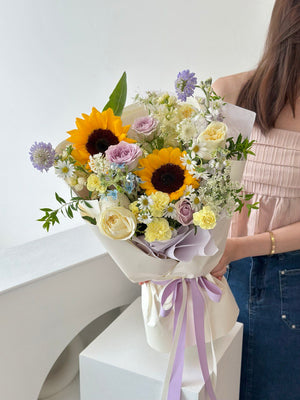 A vibrant sunflower bouquet with soft purple, yellow, and white blooms – perfect for celebrating a joyful graduation moment.