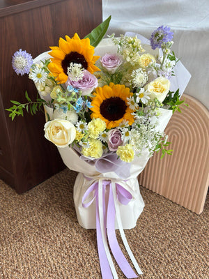 Bright sunflowers paired with pastel roses and delicate fillers, beautifully wrapped with lavender ribbon – ideal for university graduation gifts.