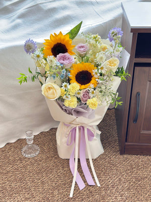Elegant and colorful sunflower arrangement wrapped in soft white and purple paper – a stunning floral gift for graduates.