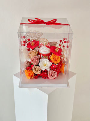 A man displays a clear box with a lucky cat figurine and flowers, intended as a gift for his friend's business launch.
