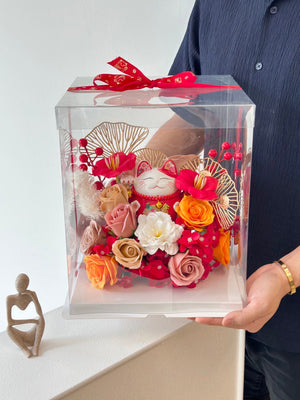 A man holds a clear box containing a business lucky cat figurine and flowers, celebrating his friend's business opening.