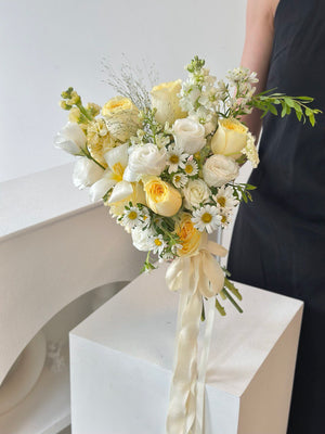 Fresh and airy bridal bouquet made with buttercup roses, white lisianthus, daisies, and textured greens – perfect for a spring or garden wedding.