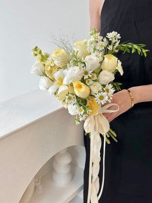 Bouquet of white and yellow flowers for bridal held by a person against a neutral background