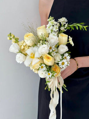 Handheld bridal bouquet with pastel roses, lush white flowers, and whimsical greenery, wrapped in trailing ivory ribbons.