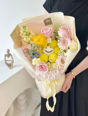 A woman in a black dress smiles while holding a mixed bouquet of flowers mix with smiley ping pong on her graduation day.