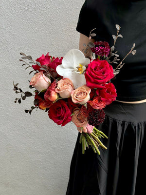 A girl in a black dress stands at Thian Hou Temple, holding a bouquet of ROM red roses for her wedding.