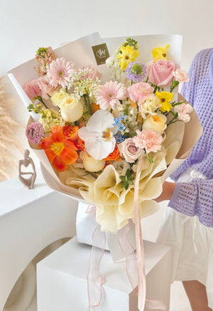 A girl in a purple cardigan holds a colorful bouquet of flowers in front of a white table for her birthday celebration.