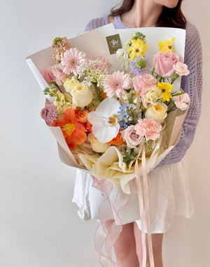 A girl wearing a purple cardigan holds a bright bouquet of flowers in front of a white table, marking her birthday event.