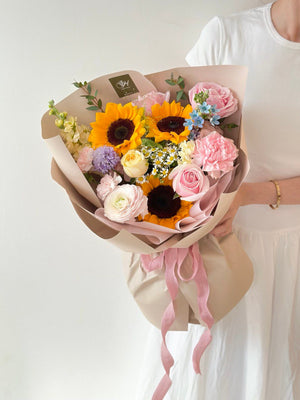 A woman in a white dress holds a bouquet of sunflowers mixed pink roses, celebrating her university graduation.