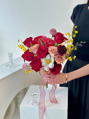 A woman in a black dress holds a wedding bouquet of red and yellow flowers at her home for a picture.