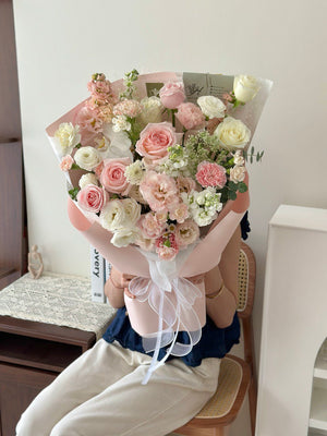 Person holding a bouquet of pink rose, white rose, white phalaenopsis and mixed of fillers in a room with a desk and chair.