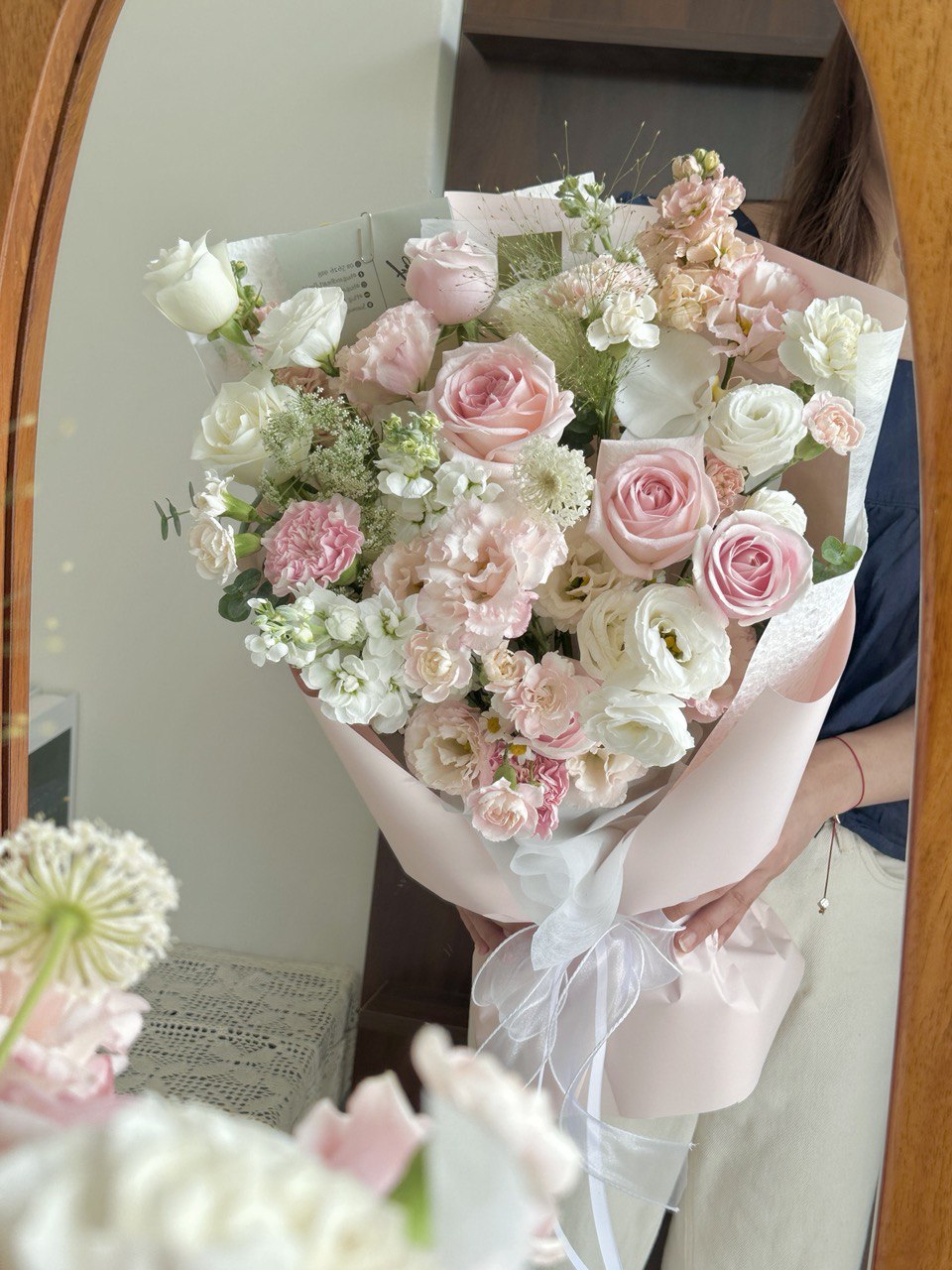 Bouquet of pink and white flowers held by a person in front of a mirror.