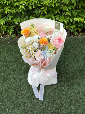 Bouquet of flowers wrapped in white paper with a pink ribbon on a grassy background