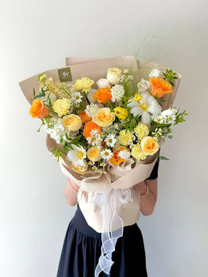 A vibrant mix of yellow-orange roses and delicate white filler flowers, beautifully arranged in a luxe wrap.